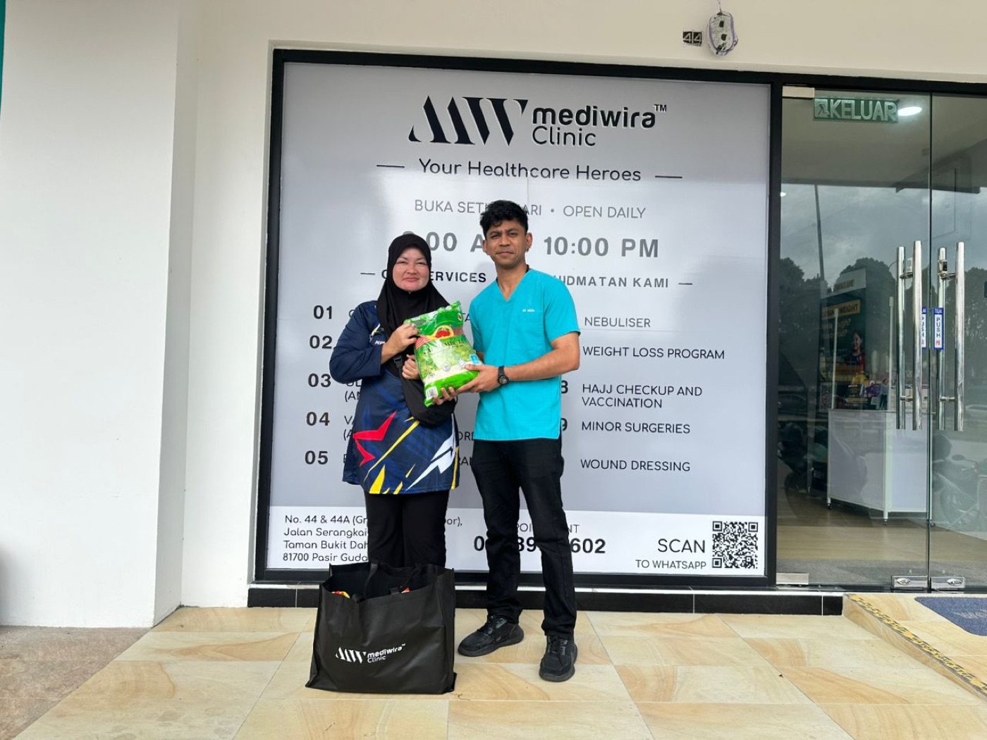 A Mediwira team member handing a bag of rice and a grocery pack to a resident outside Mediwira Clinic Pasir Gudang